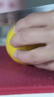 Kırpılmış sarı limonu, pembe kesme tahtasındaki bıçakla ikiye bölme görüntüsü, bulanık sırtlı sebzeleri kesme manzarası, mutfakta yemek hazırlama manzarası