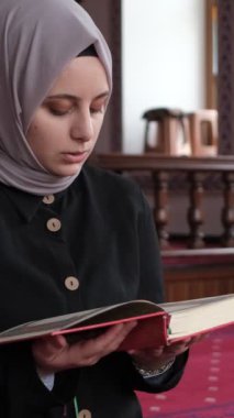 Genç Müslüman kadın caminin içinde Kuran okuyor, ahşap kürsüde el-Kuran okuyor ve içeride diz çöküp dua ediyor.