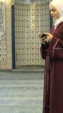 İslam İlmihal Uygulaması, camideki tesettürlü kızın elinde yeşil ekranı gösterme, telefonda İslam uygulamalarının tanıtımı 