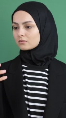 Yeşil telefon ekranına bakan Müslüman bir kadın, izole edilmiş yeşil arka plan önünde akıllı telefon gösteren genç bir kız, gülümseme.