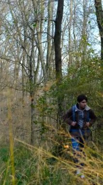 Sırt çantalı genç bir adam sonbaharda bir dağda çimlerin ve ağaçların arasında yürüyor. Genç bir kampçı ormandaki yabani otların arasında yürüyor.