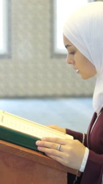 Müslüman kadın Lectern 'de okuyor, Asyalı Müslüman kız diz çöküp Kuran okuyor, Asyalı başörtüsü kızı camide Kur' an okuyor.