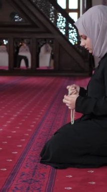 Müslüman bir kadın elleriyle boncukları sayıyor, tesettürlü bir kadın camide dizleriyle oturuyor ve dhikr okuyor.