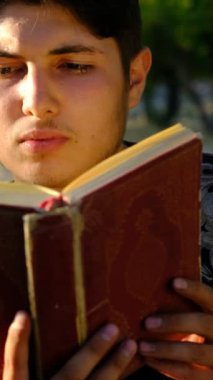 Genç adam Kuran 'ı açık havada okuyor, Kuran' ı doğada okuyor, açık havada kitap okuyor, doğa bahçesinde ibadet ediyor.
