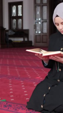 Genç Müslüman kadın caminin içinde Kuran okuyor, ahşap kürsüde el-Kuran okuyor ve içeride diz çöküp dua ediyor.