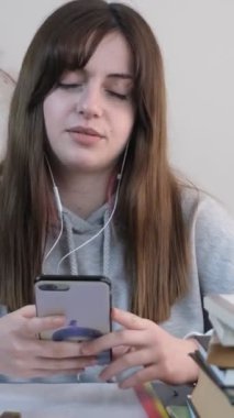 Çalışırken müzik dinleyerek mola veren genç bir kız, ev ödevine ara veriyor, kulaklıkla müzik dinleyerek derslerine ara veriyor.