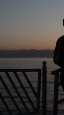 İşten sonra gün batımına doğru yürüyen şapkalı güzel bir kadın, deniz kenarında dinlenen bir kadın silueti.