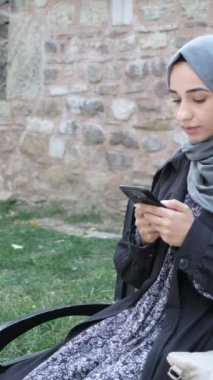 Müslüman kadın sosyal medyada cep telefonuyla vakit geçiriyor, telefonla iletişim kuruyor, dışarıda vakit geçiriyor.