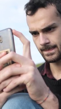 Parkta telefonlarına bakan gençlerin görüntüsü, güneşli bir günde çimlerin üzerinde boş zaman aktivitesi, dışarıdaki mesajlar, parktaki akıllı telefonlar.