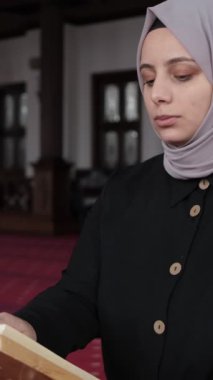 Kafiyeli kadın caminin içinde Kuran okuyor, kürsüde el-Kuran 'a dua ediyor, İslam' ın kutsal kitabını okuyor.