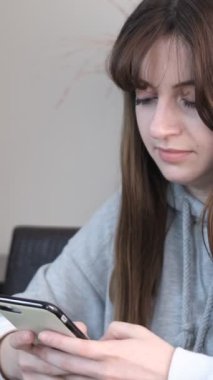 Çalışma masasında telefonuna bakan genç bir kızın görüntüsü. Ev ödevlerine ara veriyor, tatilde telefonuyla uğraşıyor.