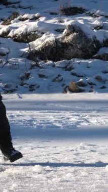 Donmuş gölde baltasıyla suya ulaşmak için buzun en üst katmanını kıran ve kendine bir su birikintisi oluşturan genç adam tasviri.