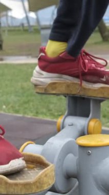 Yakın plandan çekilen denge takviye cihazıyla çalışmak, kamu spor ekipmanları üzerine spor yapmak, gençlerin belediye parklarında sağlık aktiviteleri yapmak ve müzik dinlemek.