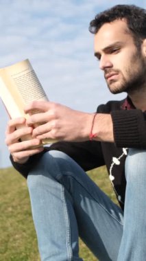 Çimlerin üzerinde kitap okuyan, güneşli bir günde çimenlerde roman okuyan güneşli bir günde parkta boş vakit geçiren yalnız bir adamın görüntüsü.