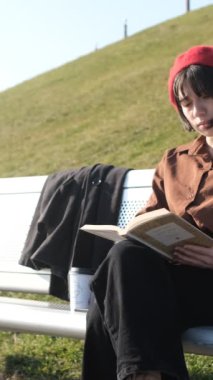 Genç ve çekici bir kadın bankta kitap okumaktan hoşlanır. Açık havada eğlenirken temiz havada bir kitapla ilgilenir..