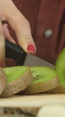 Tahta sunum tahtasında yeşil kivilerin dilimlenmesi, kadının kiviyi yakından kesmesi, tematik taze meyve hazırlama, ahşap sunum tabağında dilimleme işlemi.