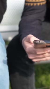 Güneşli bir günde beyaz bankta sadece elleri görünen telefonla uğraşmanın, parkta telefonda oyun oynamanın görüntüsü.