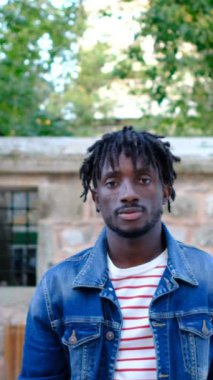 Genç siyahi Afrikalı bir adam kameranın önünde duruyor sağ yumruğunu havaya kaldırıyor, siyah bir genç kameraya bakıyor.