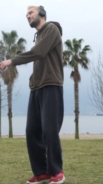 Genç adam parkta tek başına dans ediyor, eğleniyor, çimenlerde müzik dinleyerek eğleniyor.
