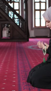 Müslüman bir kadın elleriyle boncukları sayıyor, tesettürlü bir kadın camide dizleriyle oturuyor ve dhikr okuyor.