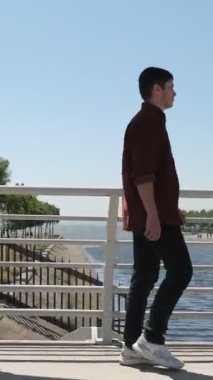 Beyaz korkuluk köprüsünde yürüyen yakışıklı bir adam, güneşli bir günde bir öpücükle nehri geçerken, yolcu köprüsünü geçerken.