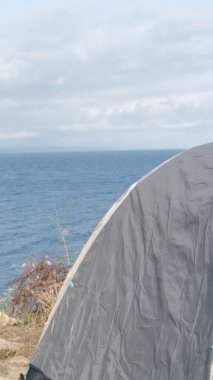 Exit from the camping tent, camping boy in white t-shirt coming out of tent, tent set up against sea view, view of young male vacationing in tent