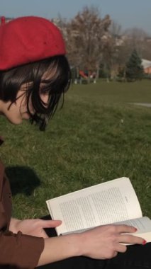 Genç, güzel bir kadın çimenler üzerinde kitap okumaktan, güneşli bir pazar günü açık hava aktivitesinden, temiz hava ile ilgili bir kitapla ilgilenmekten hoşlanıyor.