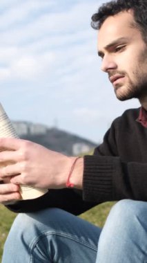 Çimenler üzerinde kitap okuyan, güneşli bir günde çimlerin üzerinde roman okuyan, güneşli bir günde parkta boş vakit geçiren yalnız bir adamın görüntüsü.