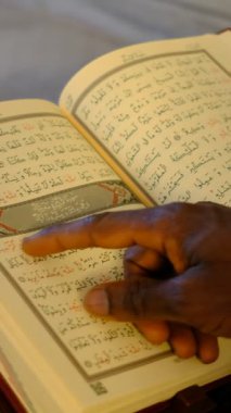 Siyahi bir genç, Kuran 'ın çizgilerini parmaklarıyla takip eder. Arap alfabesi ile birlikte dini kitap Kuran' dır.