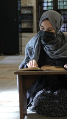 Maskeli Müslüman kadın Kuran okuyor, tesettürlü kız Kuran 'dan ahşap kürsüde kitap okuyor, camide Kuran okuyor.