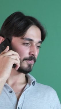 Konuşan genç beyaz adam gülümsüyor yeşil ekranın önünde akıllı telefondan konuşuyor, insanlar konuşmak için telefon kullanıyor.