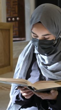 Maskeli Müslüman kadın Kuran okuyor, tesettürlü kız caminin içinde dua ediyor, müslüman kız İslam kurallarına göre kitap için dua ediyor.