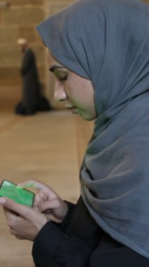 İslami cami çekimlerinde yeşil ekran akıllı telefon kullanan sadık Müslüman kız camideki telefondan internetten kitap okuyor.