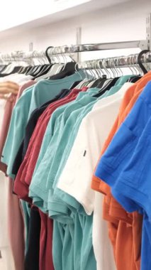 Young shopper looking at the products in the aisle one by one, to examine the colorful clothes hanging on the hanger one by one