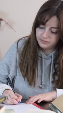 Masasında yoğun bir şekilde ders çalışan, kitap ve kalemlerden oluşan ödevlerini yapan, sınavlara sıkı hazırlanan bir kız resmi