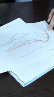 Tezgahtarlar kağıtlardaki grafiği yorumlarken, esnaf da çalışma masasında istatistiksel belgeyi inceliyor.