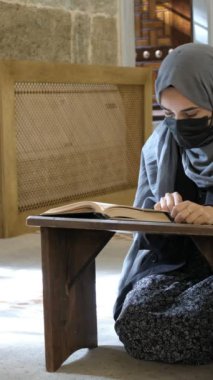 Maskeli Müslüman kadın Kuran okuyor, tesettürlü kız caminin içinde dua ediyor, Müslüman kız diz çöküp Kuran 'a dua ediyor.