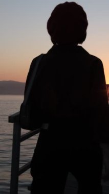 İşten sonra gün batımına doğru yürüyen şapkalı güzel bir kadın, deniz kenarında dinlenen bir kadın silueti.