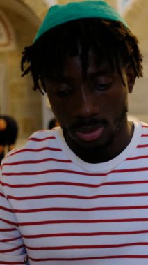 Kafasında dini şapkası olan Afrikalı genç bir adam camide oturmuş, Müslüman erkekler camide ibadet ediyor.