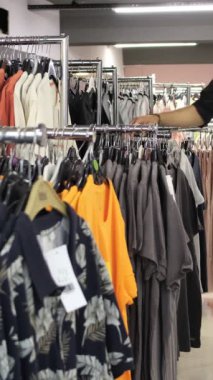 Man looking t-shirt in store, young man examining t-shirts in aisle, image of inspecting clothes on hangers, teenager shopping