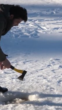 Donmuş gölde baltasıyla suya ulaşmak için buzun en üst katmanını kıran ve kendine bir su birikintisi oluşturan genç adam tasviri.