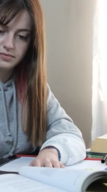 Kitapların arasında okuyan öğrenci, üst üste dizilmiş kitap ve defterlerle dolu masa, sınavlara hazırlanan genç kız.