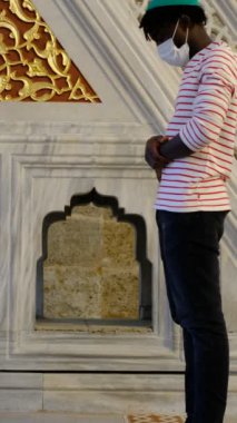 Siyahi Müslüman genç adam camide namaz kılıyor. Yüzünde maske olan Afrikalı bir genç ibadet ediliyor. Müslüman erkekler camide dua ediyor.