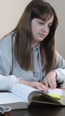 Kitapların arasında okuyan öğrenci, üst üste dizilmiş kitap ve defterlerle dolu masa, sınavlara hazırlanan genç kız.