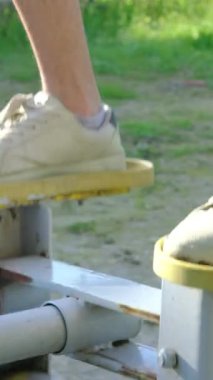 Açık hava parkında spor yapan genç bir adamın ayaklarının yakın çekim görüntüsü. İnsanlar parkta bulunan spor malzemelerini kullanıyorlar.