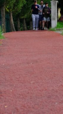 Yürüyüş yolunda koşan üç genç adam, parkta spor yapan gençlerin farklı açılardan görünüşü