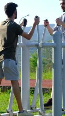 Parktaki spor aletleri üzerinde egzersiz yapan iki genç arkadaşın arka plandaki görüntüleri. İnsanlar sosyal parklarda spor aktiviteleri yapıyor.