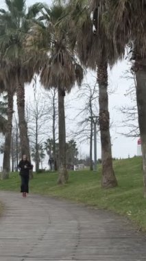 Palmiye ağaçlarıyla kaplı plaj bandında koşan genç adam, sonbaharda müzik dinleyerek tempoda koşuyor.