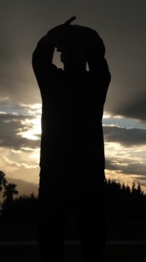 Parkta güneşe doğru uzanan, doğada spor yaparak formunu koruyan genç bir adamın silüeti.