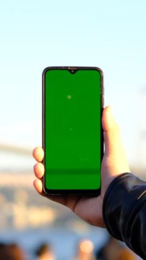 A tourist hold on his hand across the bridge landscape, the young man hold in front of the cityscape while green screen smartphone Besiktas Istanbul